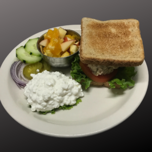 picture of tuna salad sandwich on wheat toast with lettuce and tomatoes. with a side of cottage cheese, fresh fruit, cucumbers, and red onions